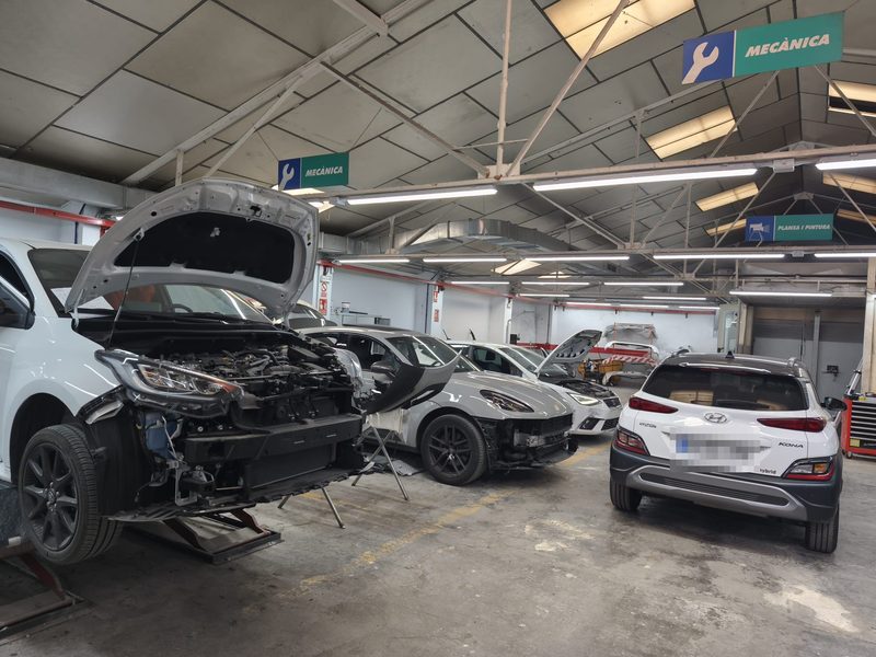 Nau del taller amb vehicles en reparació i la zona de mecànica